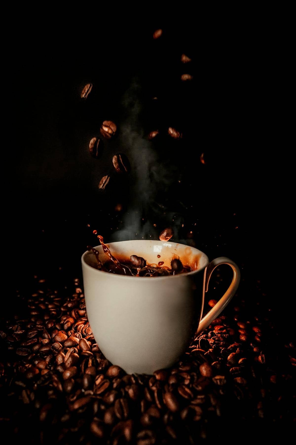 Tasse de café fumante, grains en suspension sur fond noir